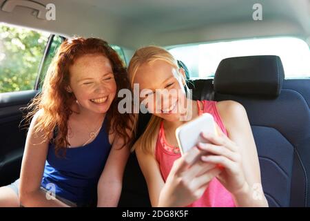 Heureux préteen fille amis prenant selfie dans le siège arrière de voiture Banque D'Images
