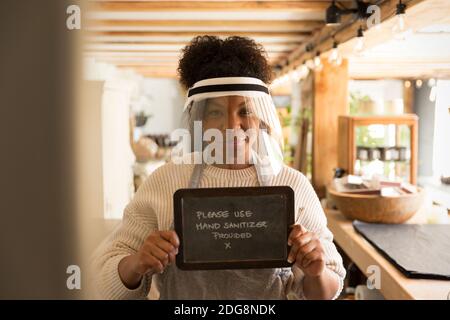 Portrait d'une femme propriétaire d'atelier dans un écran facial tenant l'assainisseur pour les mains signe Banque D'Images