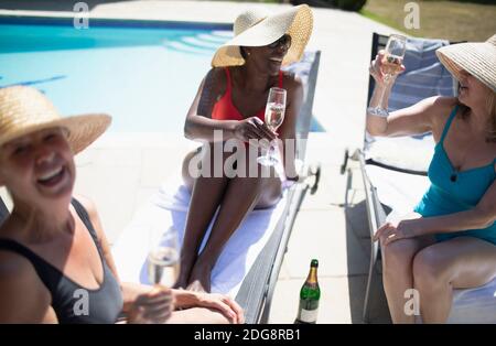 Des femmes heureuses et séniors qui boivent du champagne au bord de la piscine en été Banque D'Images