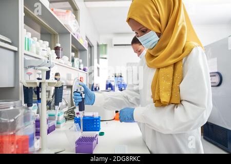 Scientifique féminine en hijab et masque facial à l'aide d'une pipette laboratoire Banque D'Images