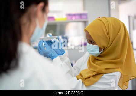 Scientifique féminine en hijab et masque facial avec plateau à échantillons Banque D'Images