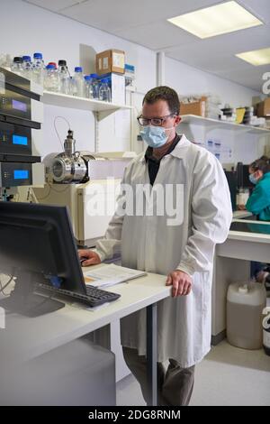 Homme scientifique dans le masque facial utilisant l'ordinateur en laboratoire Banque D'Images