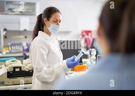 Scientifique féminine en masque facial examinant l'échantillon en laboratoire Banque D'Images