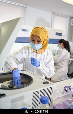 Scientifique féminine en hijab et masque facial utilisant la centrifugeuse dans laboratoire Banque D'Images