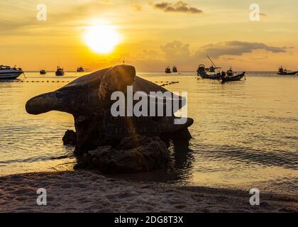 Koh Tao, Thaïlande: Avril 23 2019: statue de tortue de mer de village d'île sur la côte de plage, beau coucher de soleil, trafic de bateau de long conte dans l'eau. Banque D'Images