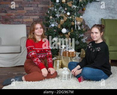 Deux filles joyeuses sont assises sous un arbre de Noël décoré Banque D'Images