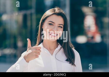 Photo de douce charmante jeune femme habillée blanc chemise formelle sourire en montrant le pouce vers le haut à l'extérieur Banque D'Images