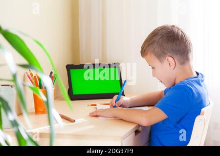 Joli dessin d'écolier, tablette avec écran vert rester sur le bureau. Concept d'éducation et d'apprentissage à distance. Banque D'Images