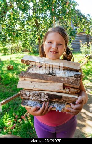 Une petite fille en tricot chandail tenant le bois de chauffage dans ses mains. Banque D'Images