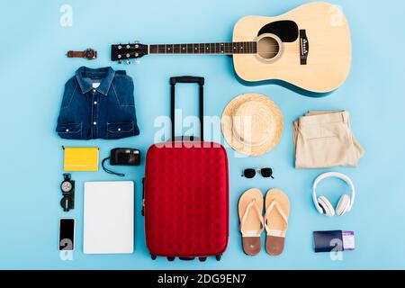 vue de dessus des lunettes de soleil, des vêtements, des accessoires et des appareils près des bagages rouges sur le bleu Banque D'Images