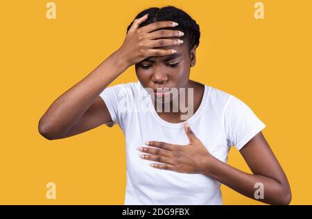 Femme africaine malade ayant de la fièvre et de la toux sur fond jaune Banque D'Images