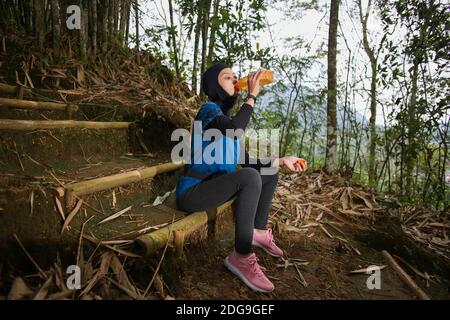 Attirante sportive asiatique musulmane portant le hijab à l'extérieur, assis, de l'eau potable Banque D'Images