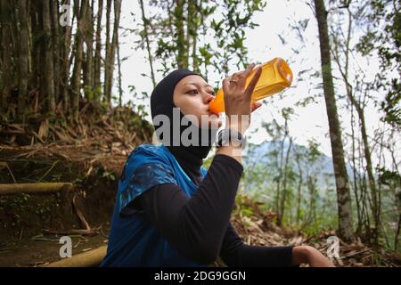 Attirante sportive asiatique musulmane portant le hijab à l'extérieur, assis, de l'eau potable Banque D'Images