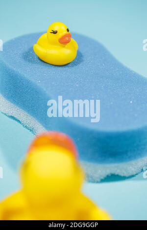 Petit et grand canard en caoutchouc jaune sur le dessus de l'éponge de bain bleue, sur fond bleu, concept de nettoyage et de bain Banque D'Images