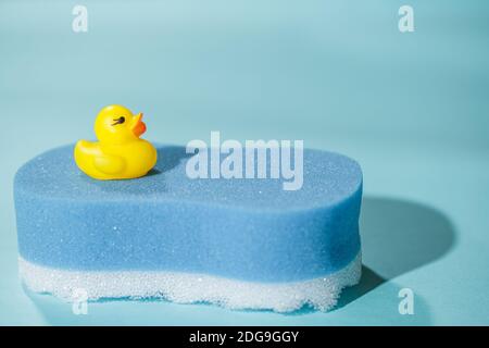 Petit canard en caoutchouc jaune sur éponge de bain bleue, sur fond bleu, concept de nettoyage et de bain Banque D'Images