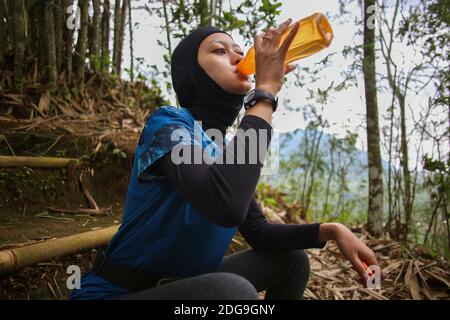 Attirante sportive asiatique musulmane portant le hijab à l'extérieur, assis, de l'eau potable Banque D'Images