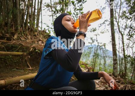 Attirante sportive asiatique musulmane portant le hijab à l'extérieur, assis, de l'eau potable Banque D'Images