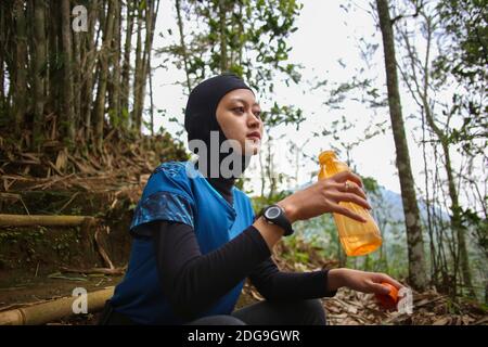 Attirante sportive asiatique musulmane portant le hijab à l'extérieur, assis, de l'eau potable Banque D'Images