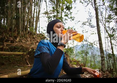 Attirante sportive asiatique musulmane portant le hijab à l'extérieur, assis, de l'eau potable Banque D'Images