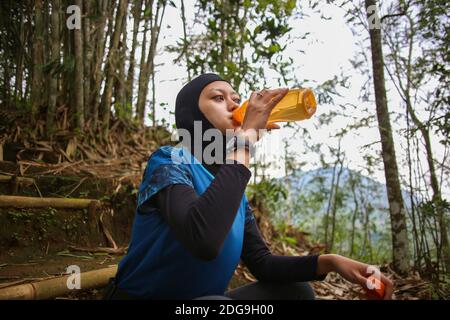 Attirante sportive asiatique musulmane portant le hijab à l'extérieur, assis, de l'eau potable Banque D'Images