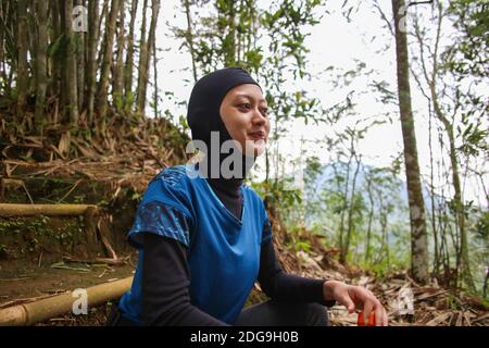 Attirante sportive asiatique musulmane portant le hijab à l'extérieur, assis, de l'eau potable Banque D'Images