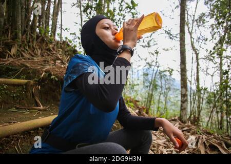 Attirante sportive asiatique musulmane portant le hijab à l'extérieur, assis, de l'eau potable Banque D'Images