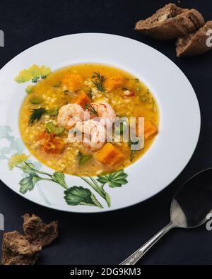 Soupe de potiron avec bulgur, crevettes, céleri et aneth. Baguette de seigle assaisonnée à l'ail. Banque D'Images