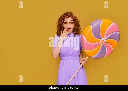 Wow, c'est le monde des grands sucettes sucrées. Drôle de jeune femme fait un visage surpris et tient un grand lollipop dans ses mains Banque D'Images