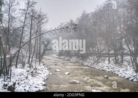 L'eau sale du fleuve passant après une forte chute de neige et sa promenade sur les côtés à Merano, en Italie, couverte de neige humide. Banque D'Images