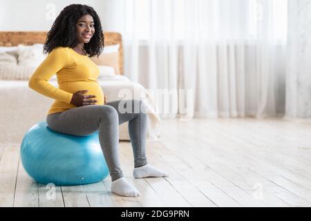 Femme enceinte souriante qui fait de l'exercice sur le ballon de fitness Banque D'Images