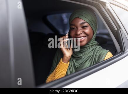 Femme musulmane noire voyageant en voiture sur le siège arrière et parlant sur le téléphone portable Banque D'Images