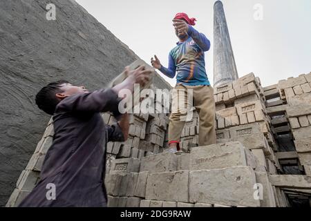 Après le séchage des briques d'argile brute, elles sont empilées à l'intérieur d'un four de briques à cheminée fixe le long de la rivière hazy Turag à Asulia au Bangladesh. La zone est remplie de fours de briques à cheminée fixe, qui viennent de transformer leur production en grande vitesse. Pendant la plus grande partie de l'année, les fours en briques sont inondés car ils sont situés sur les lits de la rivière. Lorsque l'eau recule pendant la saison sèche, les fours reviennent à la vie alors que des centaines d'ouvriers empilent des briques fraîchement pressées en silt dans d'énormes fours à bois et à charbon. En utilisant une technique simple qui remonte des centaines d'années, la cheminée fixe bric Banque D'Images