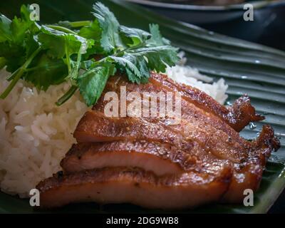 Gros plan de riz recouvert d'un col de porc frits avec concombre et coriandre sur des feuilles de banane. Cuisine thaïlandaise et asiatique. Mise au point sélective. Banque D'Images