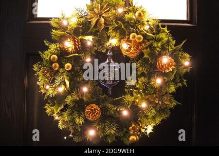 Couronne de Noël artificielle lumineuse ornée de fleurs dorées et de cônes de pin accrochés à une porte noire avec un défonceuse au centre de Manchester, en Angleterre Banque D'Images