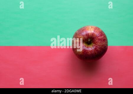 Une pomme rouge isolée sur fond demi-vert et demi-rouge. Style pop art. Plan d'affichage de la vue de dessus en bas avec espace pour le texte Banque D'Images