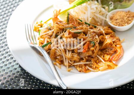 Assiette de nouilles sautées traditionnelles thaïlandaises ou thaïlandaises avec crevettes sur plaque blanche, gros plan sur le juteux Pad Thai sur plat blanc avec fourchette, belle décoration de nourriture Banque D'Images