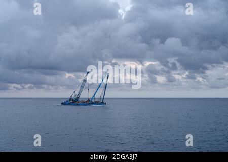 Une barge de grue de construction flotte le long de la côte pendant les travaux de remise en état des terres au large de la côte de Ligurie, en Italie Banque D'Images