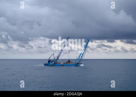 Une barge de grue de construction flotte le long de la côte pendant les travaux de remise en état des terres au large de la côte de Ligurie, en Italie Banque D'Images