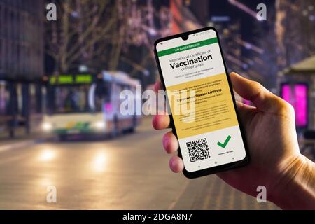 Smartphone affichant un certificat de vaccination numérique valide pour le COVID-19 dans la main d'homme, le centre-ville et le bus de ville en arrière-plan. Vaccination, maladie i Banque D'Images