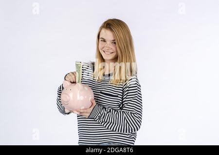 Magnifique modèle ado Blonde tenant UNE banque de Piggy contre UN Arrière-plan blanc Banque D'Images