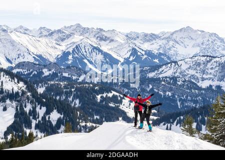 Le couple Senior fait de la randonnée en raquettes dans les montagnes d'hiver de la neige alpine. Heureux succès personnes avec les bras levés. Allgau, Bavière, Allemagne. Banque D'Images