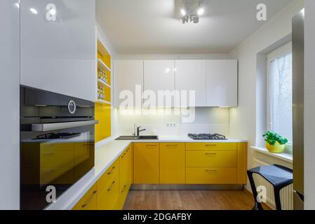 Intérieur moderne de la cuisine dans un appartement de luxe. Cuisine jaune avec comptoir blanc. Évier noir. Cuisinière à gaz. Four. Armoires et tiroirs. Banque D'Images