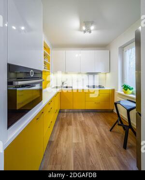 Intérieur contemporain de la cuisine dans un appartement moderne. Armoires et tiroirs jaunes. Compteur blanc. Cuisinière à gaz, four et évier. Banque D'Images