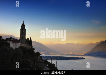 Tour de l'église sur le pic de la montagne au-dessus d'un lac alpin majeur à Dusk à Ronco sopra Ascona au Tessin, Suisse. Banque D'Images