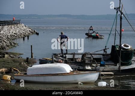 Un pêcheur se tient sur la poupe de son bateau en attendant que la marée soit suffisamment haute pour quitter Greenfield Dock, pays de Galles. Banque D'Images