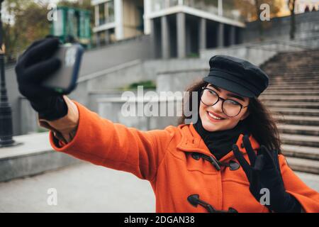 Une jeune femme portant un manteau et un chapeau prend une photo d'elle-même dans la rue Banque D'Images