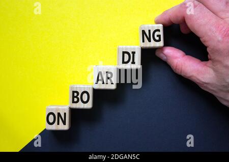 Symbole du processus d'intégration réussi. Les cubes de bois s'empilent comme escalier sur fond jaune et noir, espace de copie. Main d'homme d'affaires. Mot « Onboarding ». Banque D'Images