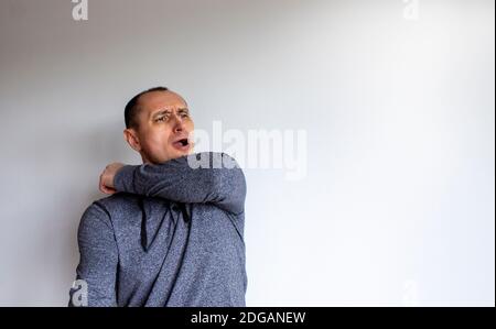 Gros plan portrait tête pétrifié jeune homme beau dans un gris éternuement sur le coude, isolé sur un magnifique fond blanc. Médical et covid- Banque D'Images