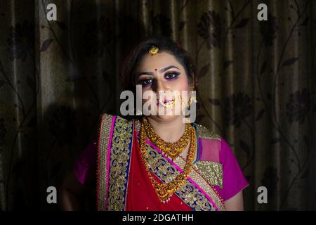 Une belle fille indienne en robe de mariée portant une saree rouge et ornements dorés Banque D'Images