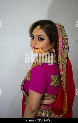 Une belle fille indienne en robe de mariée portant une saree rouge et ornements dorés Banque D'Images